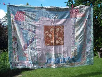 An old fashioned faded quilt made form many irregular patches hangs on a washing line in a sunny garden
